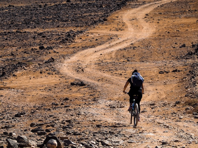 man-in-black-jacket-riding-bicycle-on-brown-sand-during-daytime